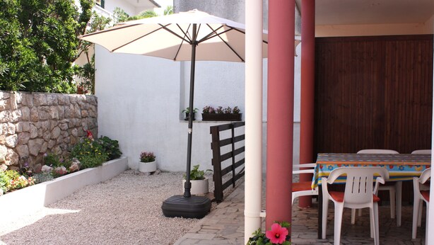 An outdoor patio area with a table and chairs, a potted plant, and a large umbrella.