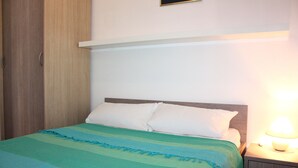 A neatly made bed with a green and blue striped bedspread, a wooden headboard, and a bedside lamp.