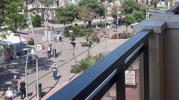 A balcony with a view of a busy street, palm trees, and a distant beach. - Sant Jordi Zeus Salou 33302 (Salou)