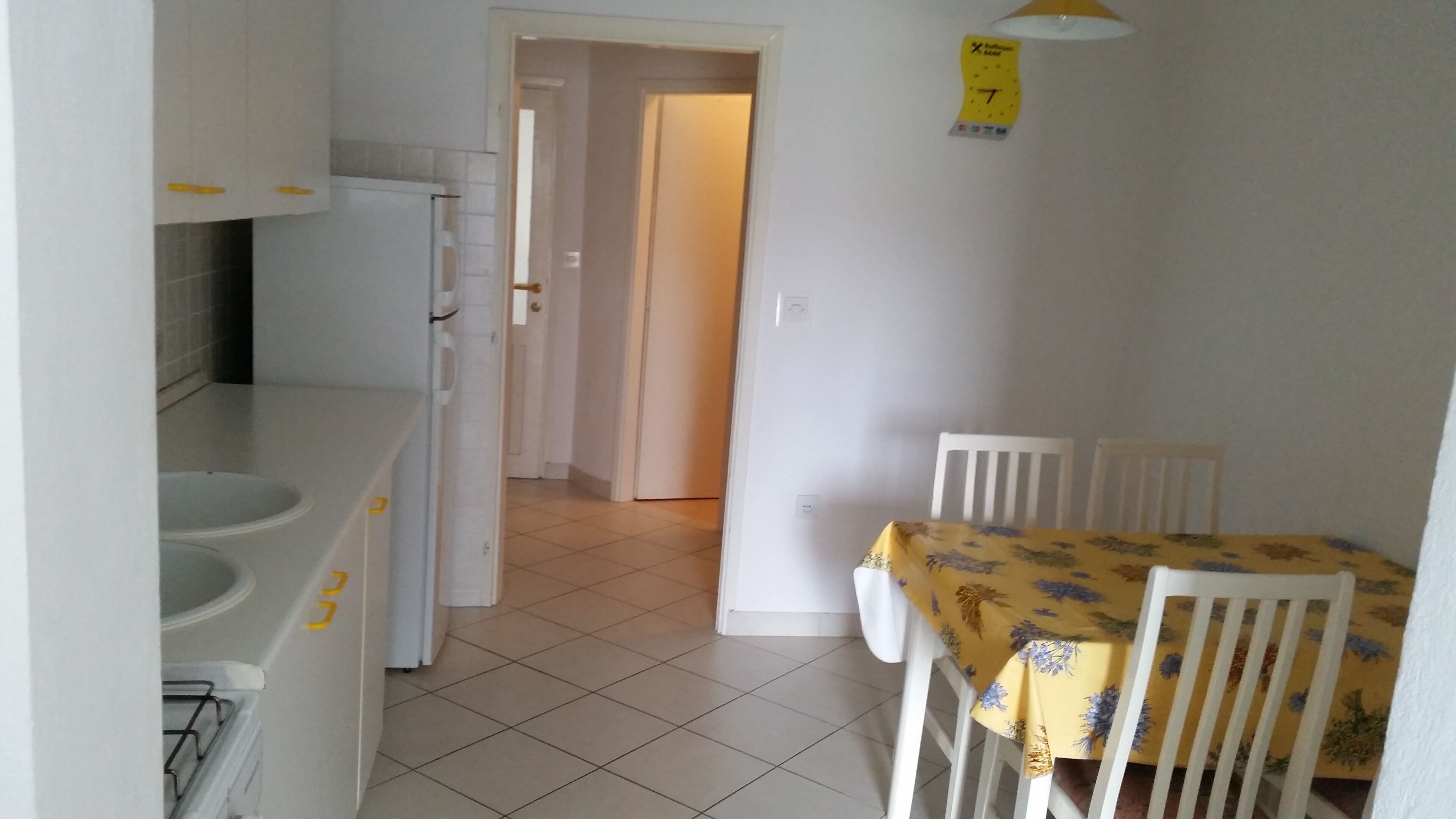 A kitchen with white cabinets, a white refrigerator, and a yellow table with floral tablecloths.
