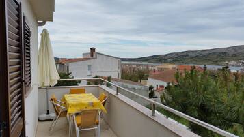 A balcony with a table and chairs, overlooking a coastal town and hills.