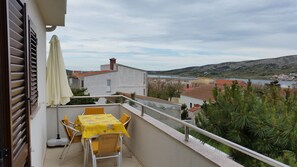 Un balcón con mesa y sillas, con vistas a un pueblo costero y colinas.