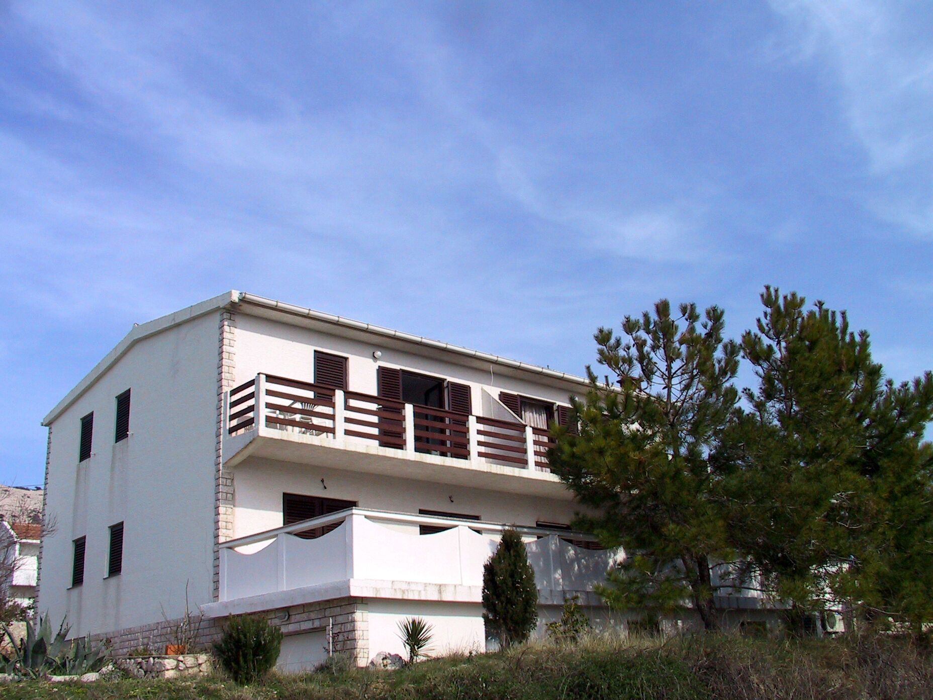 A two-story building with a balcony, a small garden area, and a clear sky.