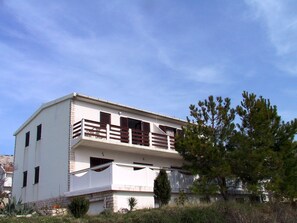 Un edificio de dos pisos con un balcón, un pequeño jardín y un cielo despejado.
