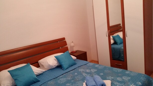 A bedroom with a wooden headboard, a bed with blue bedding, a nightstand with a lamp, and a wardrobe with a mirror. - MATILDA apartments (Pag)