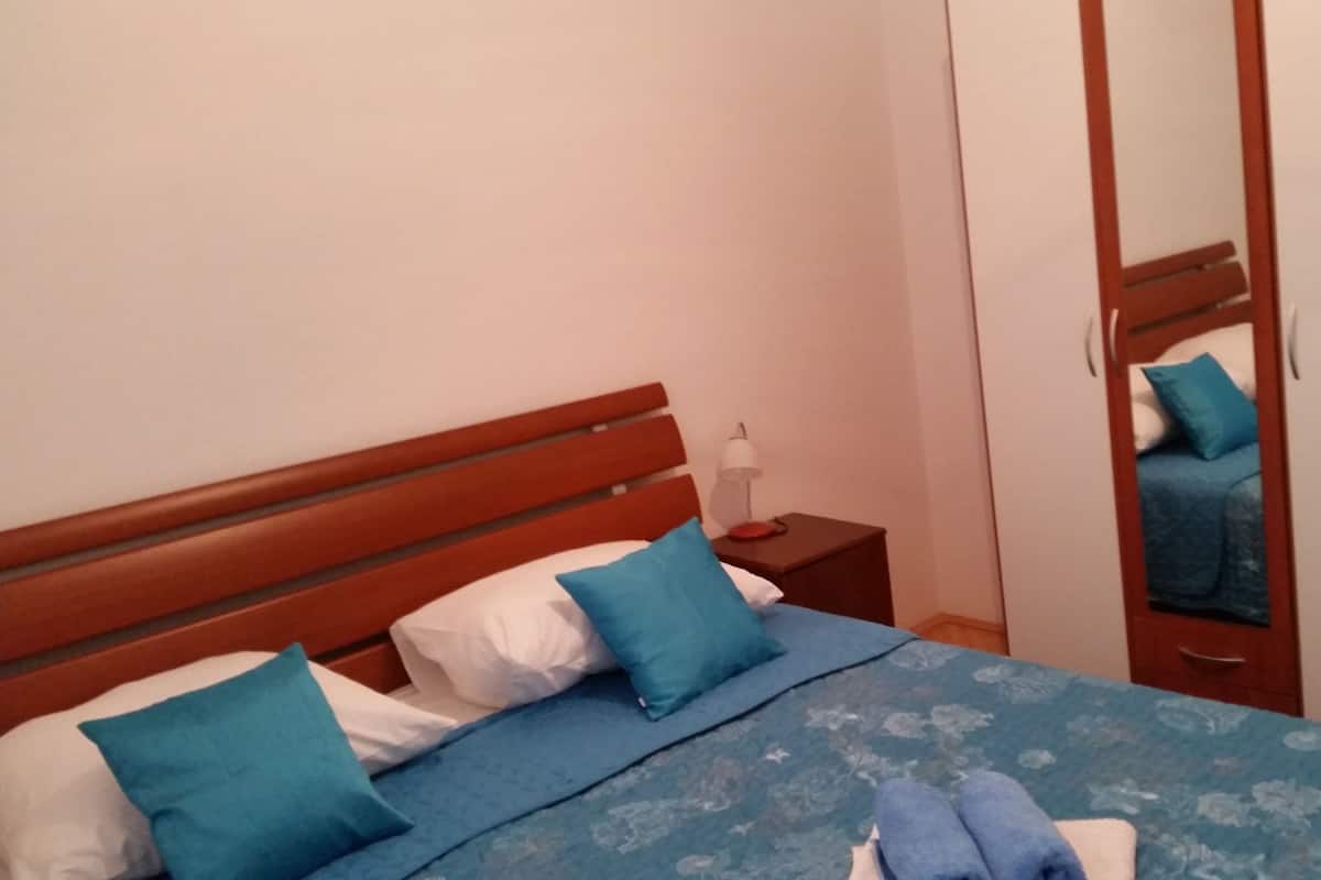 A bedroom with a wooden headboard, a bed with blue bedding, a nightstand with a lamp, and a wardrobe with a mirror.