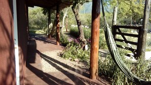 A rustic wooden structure with a dirt path leading through a garden with flowers and a hammock. - Descanso puntano (Carpintería)