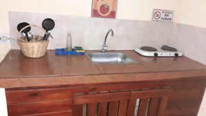 A kitchen with a wooden countertop, a sink, a stove, and a basket of utensils. - Descanso puntano (Carpintería)