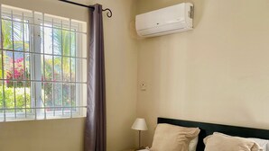Una camera d'albergo con un letto, una finestra con tende, un condizionatore d'aria e una lampada.