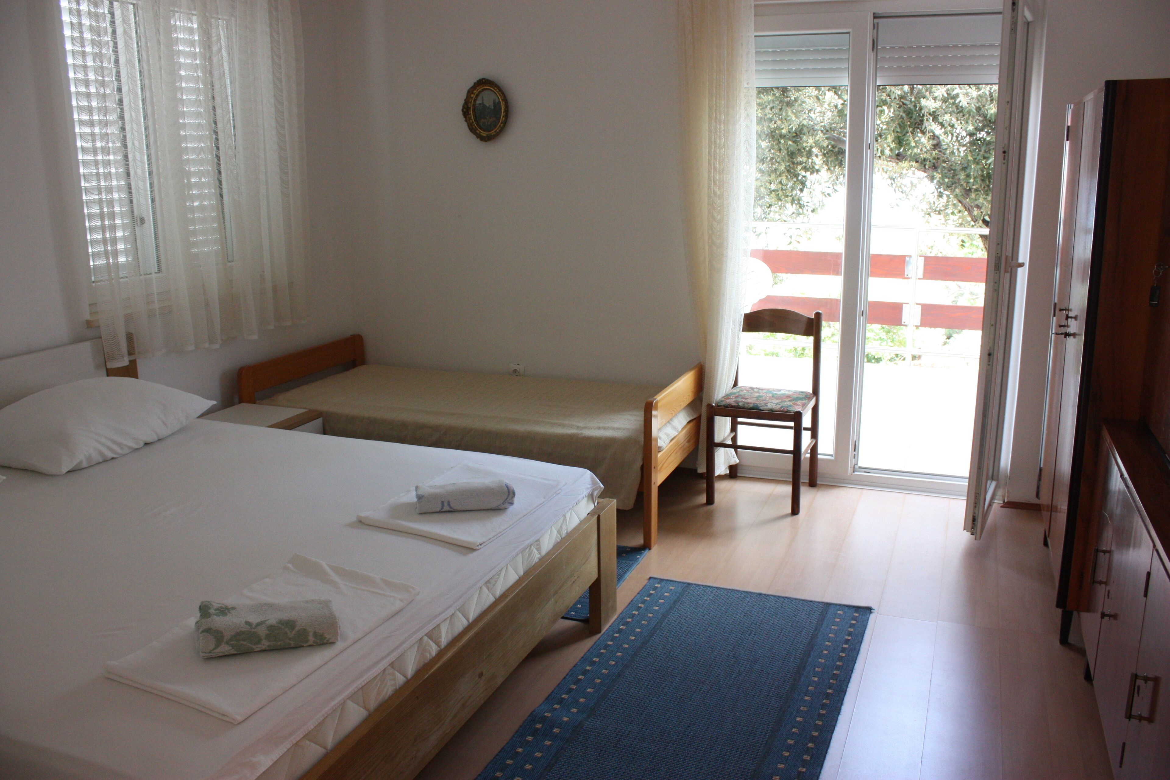 Ein Schlafzimmer mit zwei Einzelbetten, einem Holzstuhl, einem kleinen Tisch und einer Glastür, die zu einem Außenbereich führt.