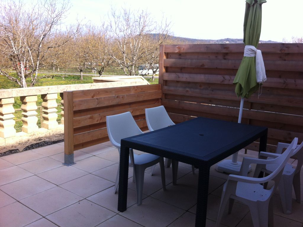En udendørs terrasse med et træbord og hvide plastikstole.