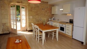 Una cocina con una mesa de madera, sillas, una lámpara colgante roja y un refrigerador blanco.