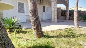 A building with a stone archway, a covered patio, and a grassy area with a tree and a plant.