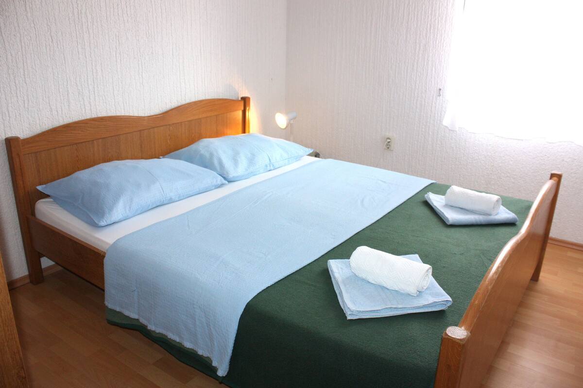 A neatly made bed with a wooden headboard, a green bedspread, and two pillows.