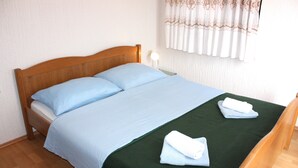 A bed with a wooden headboard, two pillows, a green bedspread, and two folded towels.