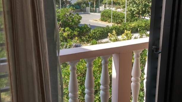 A balcony with a white balustrade, a tiled floor, and a view of a town with buildings and greenery. - Wish Apartment (Pag)