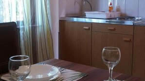 A dining table set with plates, glasses, and candles, with a kitchen in the background. - Wish Apartment (Pag)