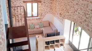 A room with a stone wall, a wooden staircase, a sofa with cushions, a wooden side table, and a window with a view. - Spectacular country house, centenary, with pool in Sencelles. (Cas Canar)