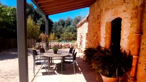 An outdoor patio with a round table and chairs, a potted plant, and a stone wall with an archway. - Spectacular country house, centenary, with pool in Sencelles. (Cas Canar)