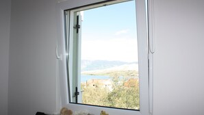 Una stanza con un'ampia finestra che si affaccia su un paesaggio suggestivo, una parete bianca e uno scaffale con oggetti decorativi.