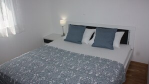Una camera da letto con un letto, una testiera bianca, due cuscini, una lampada da comodino e una coperta a motivi.