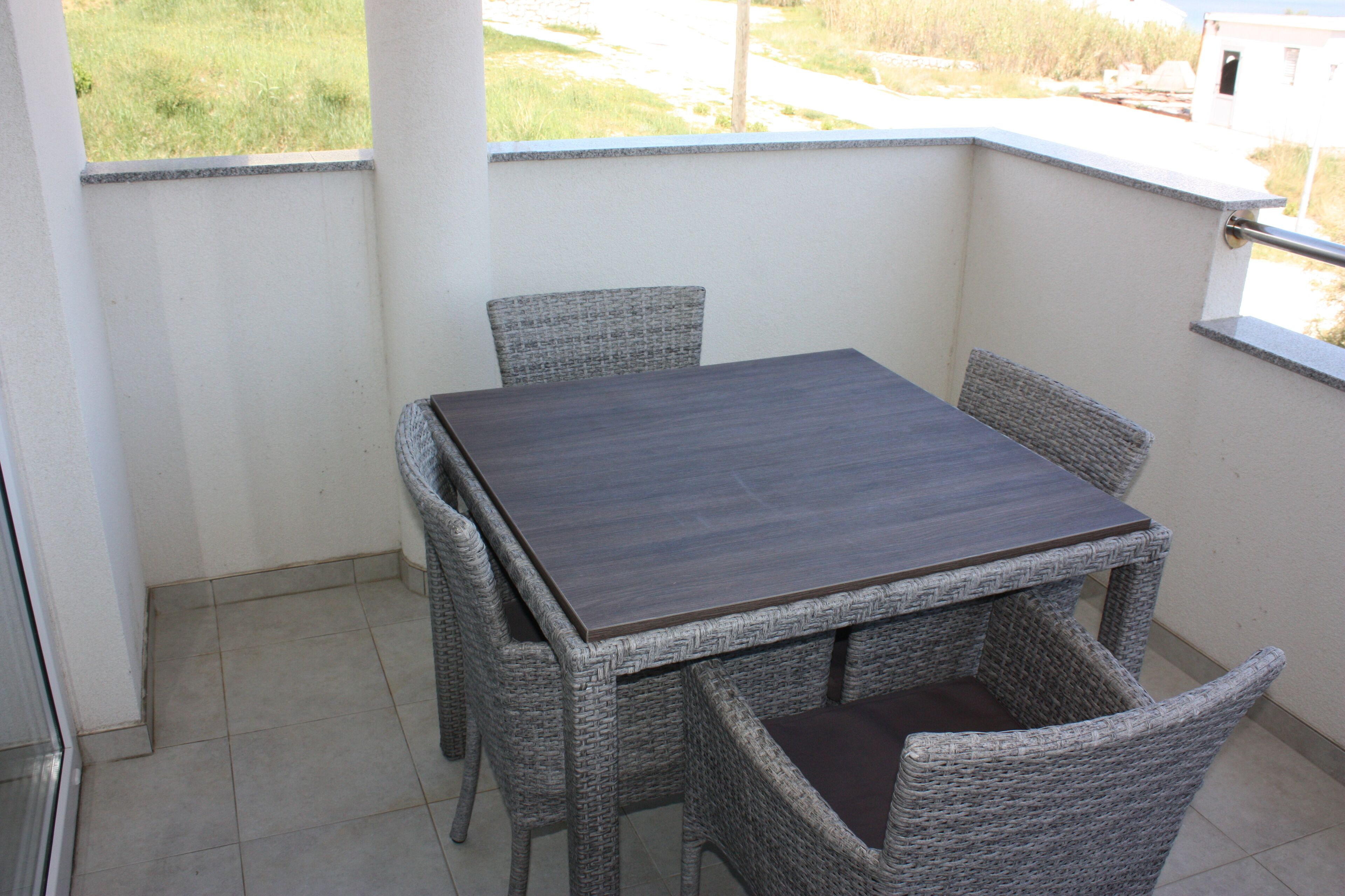 A balcony with a dark wooden table and wicker chairs.