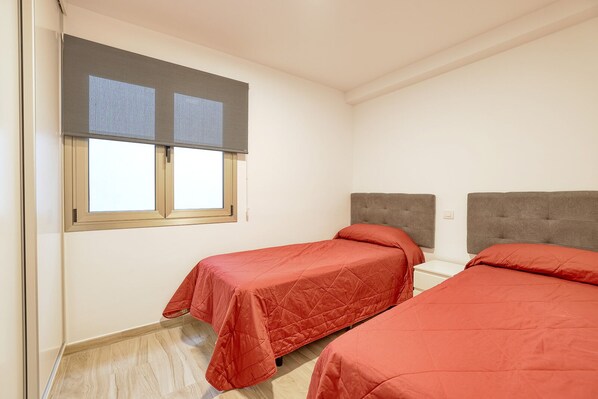 Un dormitorio con dos camas individuales, una ventana con persianas y una mesita de noche blanca.