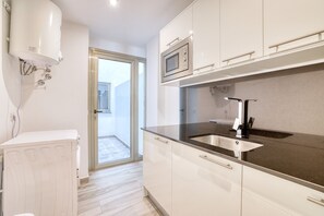 Una cocina moderna con gabinetes blancos, un lavamanos de acero inoxidable y un microondas integrado.