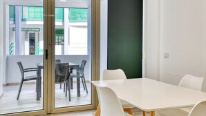 Una sala de reuniones moderna con puerta de vidrio que da a un espacio exterior, una mesa blanca y sillas de mimbre.