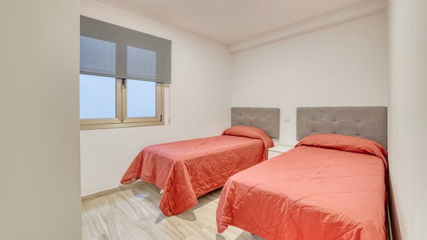 Una habitación pequeña y limpia con dos camas, una ventana con persianas y una lámpara en el techo.