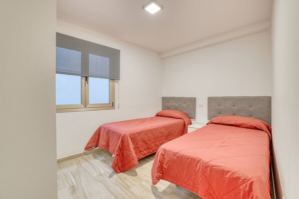 Una habitación pequeña y limpia con dos camas, una ventana con persianas y una lámpara en el techo.