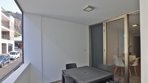 Un balcón con mesa y sillas, una puerta corrediza de vidrio y vista a la calle y edificios.