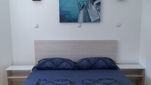 A bedroom with a bed, two bedside tables, a wall-mounted painting of sailboats, and a light-colored headboard. - Mare Apartment (Pag)