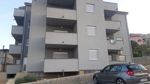 A multi-story residential building with balconies, a car parked in front, and a clear sky. - Mare Apartment (Pag)
