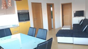 A modern living room with a sofa, a TV, and a dining area with a table and chairs. - Mare Apartment (Pag)