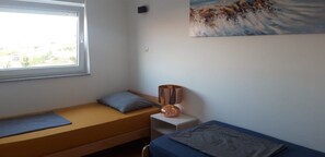 A small, single-bed room with a window, a painting on the wall, and a bedside lamp. - Mare Apartment (Pag)