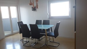 A dining area with a glass table and black chairs, a sliding glass door, and a window with natural light. - Mare Apartment (Pag)