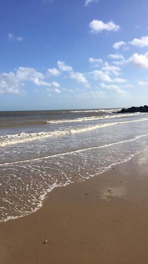 A beach with waves gently lapping onto the shore under a clear sky.