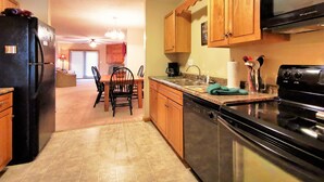 A kitchen with wooden cabinets, a black refrigerator, a stove, and a dining area with chairs and a table. - ❤️Great WiFi. Beautiful Home for a Ski Getaway. 15% off of ski rentals  (Snowshoe)