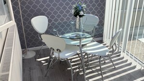 Un espacio exterior moderno para comer, con una mesa de vidrio y sillas blancas, una lámpara de metal y un muro con diseño.