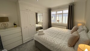 Un dormitorio con una cama grande, un armario, un espejo y una ventana con cortinas.