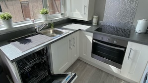 Una cocina moderna con armarios blancos, horno empotrado, lavavajillas y una ventana con plantas en macetas.
