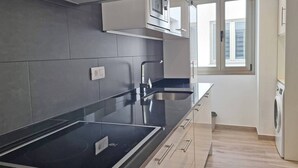 Une cuisine moderne dotée d’un plan de travail noir, d’appareils électroménagers en acier inoxydable et d’une fenêtre laissant entrer la lumière naturelle.