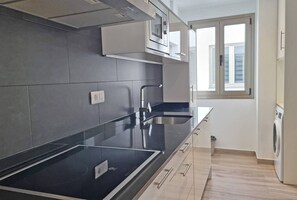 Cozinha moderna com bancada preta, eletrodomésticos de aço inoxidável e janela que permite entrada de luz natural.