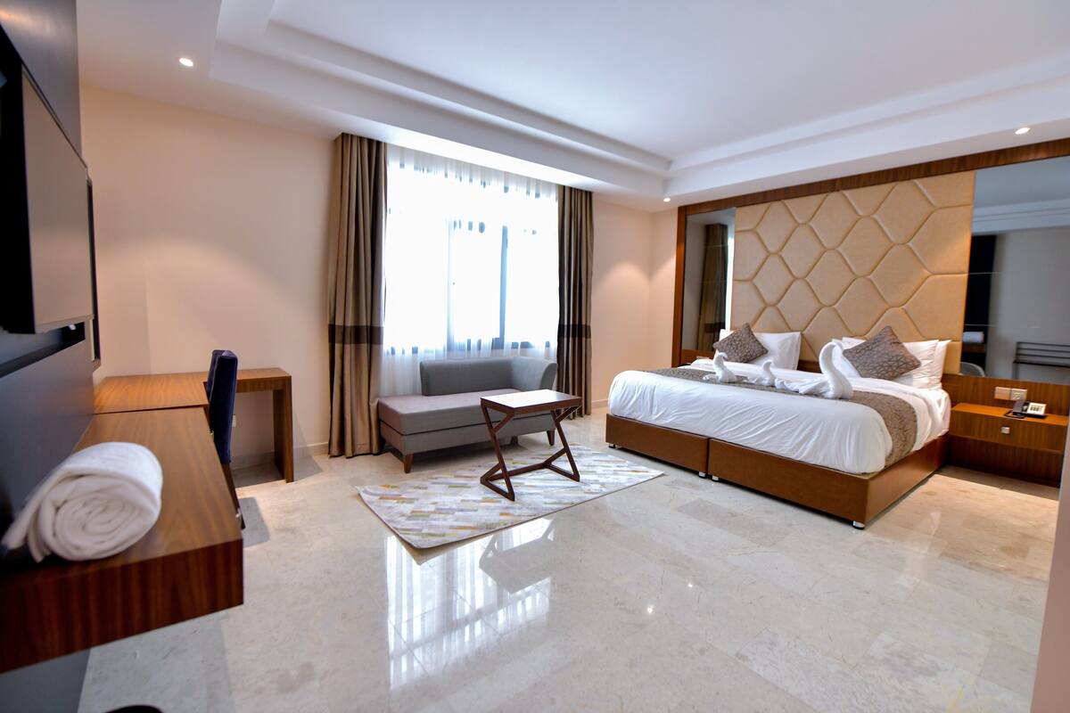 A modern hotel room with a large bed, a sofa, a small table, and a TV.