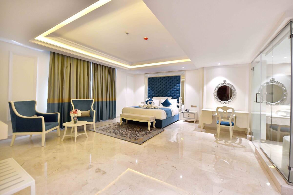 A modern hotel room with a bed, seating area, and a glass shower enclosure.