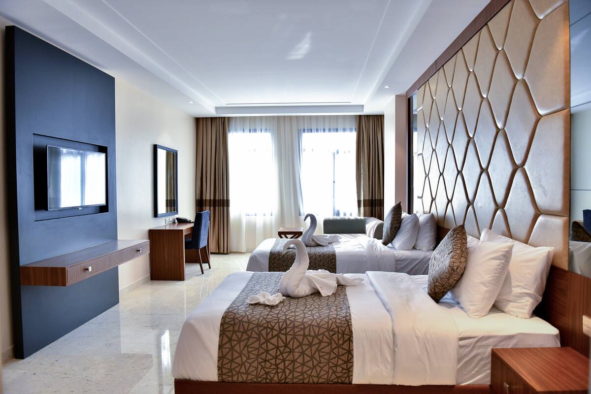 A hotel room with a large bed, a desk, a television, and a view of the outdoors.