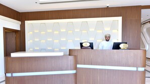 A reception desk with a modern design, featuring a wooden finish and integrated lighting. - Be Inn Hotel (Seeb)