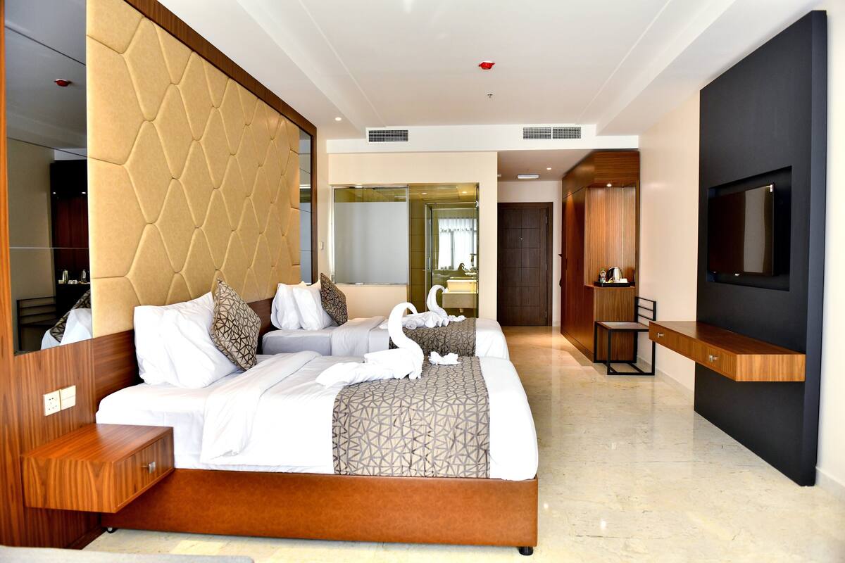 A modern hotel room with a large bed, a TV, a wooden side table, and a mirror.