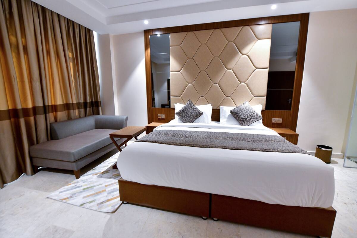 A modern bedroom with a large bed, a sofa, a wooden headboard, and a mirror.